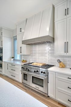 a kitchen with white cabinets and stainless steel stove top oven in the middle of it