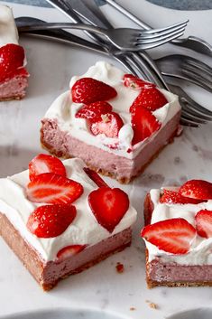 four slices of strawberry cheesecake with whipped cream and strawberries on top, next to a fork