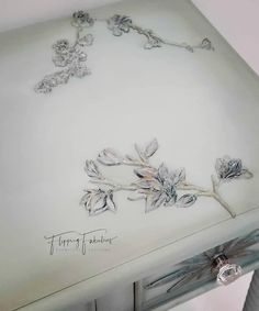 a white table with flowers painted on the top and silver trimmings around it