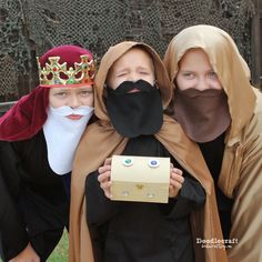 three people dressed up in costumes and masks with boxes on their heads, one holding a box while the other is wearing a mask