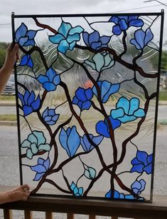 a stained glass window with blue flowers and leaves on the outside, is being held up by a woman's hand