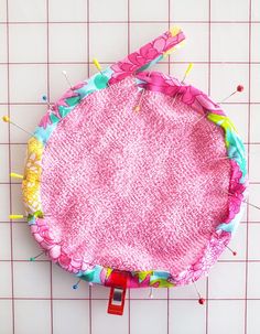 a pink piece of cloth with pins sticking out of it sitting on top of a tiled floor