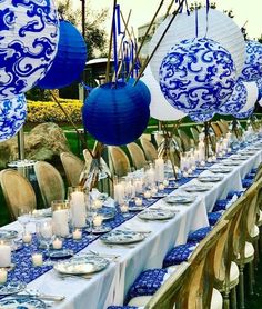 a long table set with blue and white plates, silverware and paper lantern lights