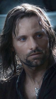 a man with long hair and blue eyes looks at the camera while wearing a black shirt