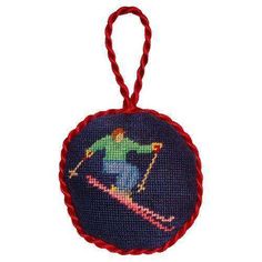 a cross - stitch ornament with a skier on it's back, hanging from a red cord