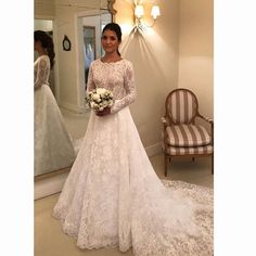 a woman standing in front of a mirror wearing a white wedding dress with long sleeves