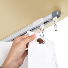 a hand holding a roll of toilet paper while hanging on a curtain rod with two clips