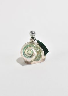 a small bottle with a green tassel on it's side and a silver ball hanging from the top