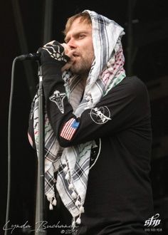 a man with a scarf on his head is singing into a microphone at an outdoor concert