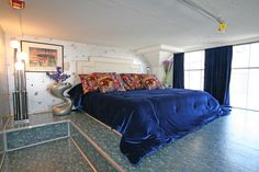 a large bed with blue sheets and pillows in a bedroom next to a glass window