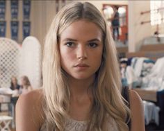 a woman with long blonde hair looking at the camera in a room full of people