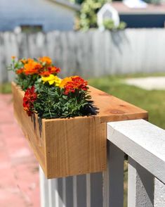 some flowers that are sitting in a wooden box on a rail outside the fenced area