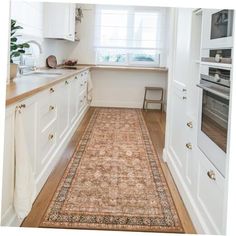 a kitchen with white cabinets and an area rug on the floor in front of the stove