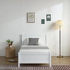 a white bed sitting on top of a wooden floor next to a lamp and rug