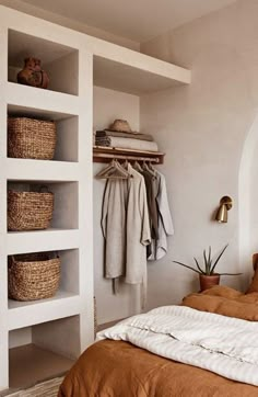 a bed sitting under a window next to a shelf filled with baskets and clothes on top of it