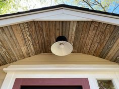 a light that is on the side of a house with wood siding and a red door