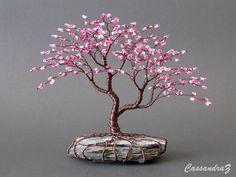 a bonsai tree with pink flowers is shown on a gray background, it appears to be in the shape of a rock