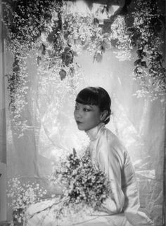 an old black and white photo of a woman with flowers in her hair sitting down