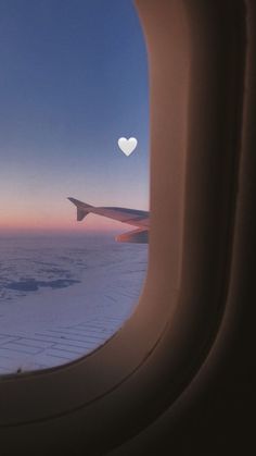 an airplane window looking out at the sky and clouds with a white heart on it