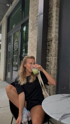 a woman sitting on a chair drinking from a glass in front of a brick building