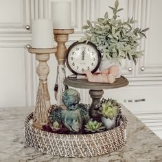 a clock sitting on top of a table next to some candles and succulents