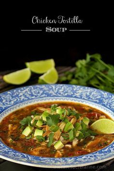 chicken tortilla soup in a blue and white bowl with limes on the side