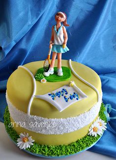 a birthday cake with a tennis player on top and daisies around the edges, sitting on a blue table cloth