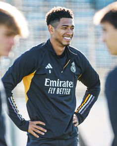 the soccer player smiles as he stands with his hands on his hips in front of other players