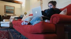 a woman sitting on a red couch with her laptop in front of her face and looking at the screen