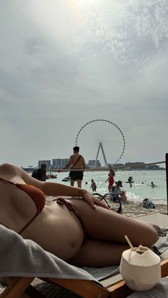 a woman laying on top of a beach chair next to the ocean and ferris wheel