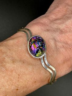 ❤Silver Plated  Cuff Bracelet with 13 x 18 mm Oval Cabochon ❤This dichroic cabochon on this bracelet is 13 x 18 mm.  The cabochon was made with multiple layers of dichroic glass, hand shaped with a diamond blade and glass grinder and fired multiple times in the kiln.  The pendant has a base layer of black and has vibrant dichroic colors of pinks, blue, green and gold dichroic shimmers.   ❤Dichroic glass is produced by stacking layers of glass and micro layers of Quartz Crystal and Metal Oxides (which are vaporized in a vacuum chamber and then applied to the surface of glass in multiple layers) to create decorative glass with shifting color structures. ❤It is difficult to capture the true beauty of Glass in photos. Dichroic Glass changes colors with different lighting and different angles, Silver Sterling Silver Oval Cuff Bracelet, Cabochon Bangle As A Gift, Cabochon Bangle Jewelry Gift, Silver Oval Cabochon Bracelet, Unique Silver Bracelet With Cabochon, Sterling Silver Cabochon Bracelets As Gifts, Silver Cabochon Bracelets For Gift, Silver Cuff Bracelet With Cabochon, Unique Silver Cuff Bracelet With Cabochon