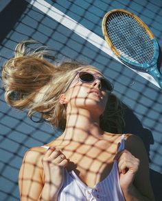 a woman wearing sunglasses and holding a tennis racquet in front of a net