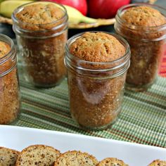 several jars filled with cookies sitting on top of a table next to bananas and apples