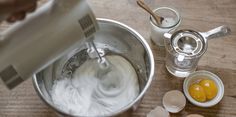 someone mixing eggs in a metal bowl on a wooden table next to other ingredients and utensils