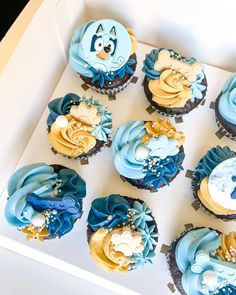 a box filled with blue and yellow cupcakes on top of a white table