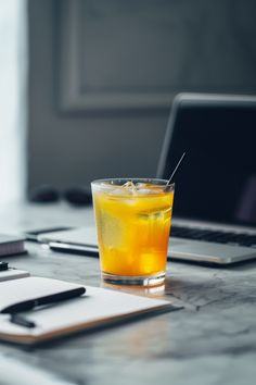 a glass filled with liquid sitting on top of a table next to a laptop computer