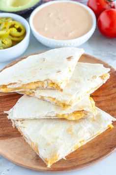 three quesadillas on a wooden plate with salsa and tomatoes in the background