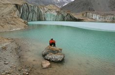 a man sitting on top of a large rock next to a body of blue water