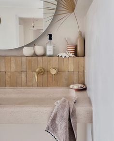 a bathroom sink under a large mirror next to a shelf with bottles and towels on it