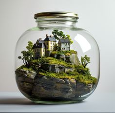 a glass jar filled with water and houses on top of a rock covered hill in front of a white wall