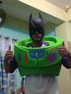 a man in a batman costume is holding up a green plastic toy bowl with his thumbs up