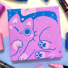 a painting of a pink cat with blue eyes on it's face, surrounded by markers and crayons