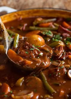 a spoon full of stew with potatoes, carrots and green beans in it is being held by a ladle