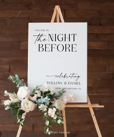 a sign that says the night before is decorated with flowers and greenery in front of a wooden wall