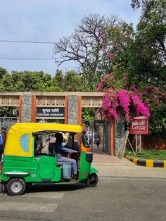 a green and yellow tuk - tuk driving down the street in front of a building