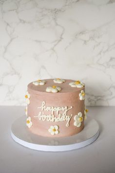 a pink birthday cake with white flowers on top and happy birthday written on the side