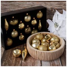 a bowl filled with gold christmas ornaments next to a black box and white tissue paper