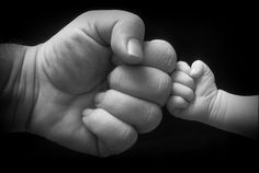 a black and white photo of a baby's hand holding the fist of an adult