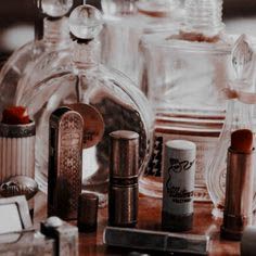 many different types of perfume bottles on a wooden table with glasses and other items around them