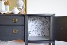 a black dresser with two drawers and some white vases on it's side